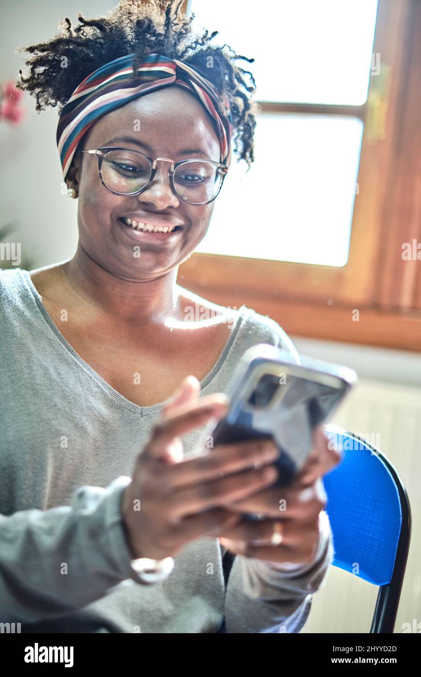 Junge schwarze Frau mit Afro-Frisur und Brille mit Mobiltelefon in einem Haus. Lifestyle-Konzept. Stockfoto