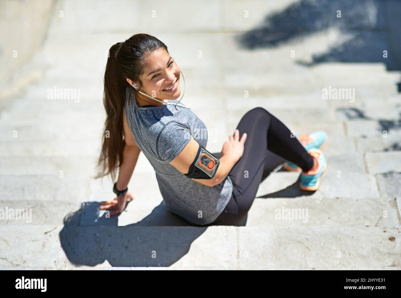 Nach dem Lauf in guter Stimmung. Aufnahme einer sportlichen jungen Frau, die Musik hört, während sie draußen auf einer Treppe sitzt. Stockfoto