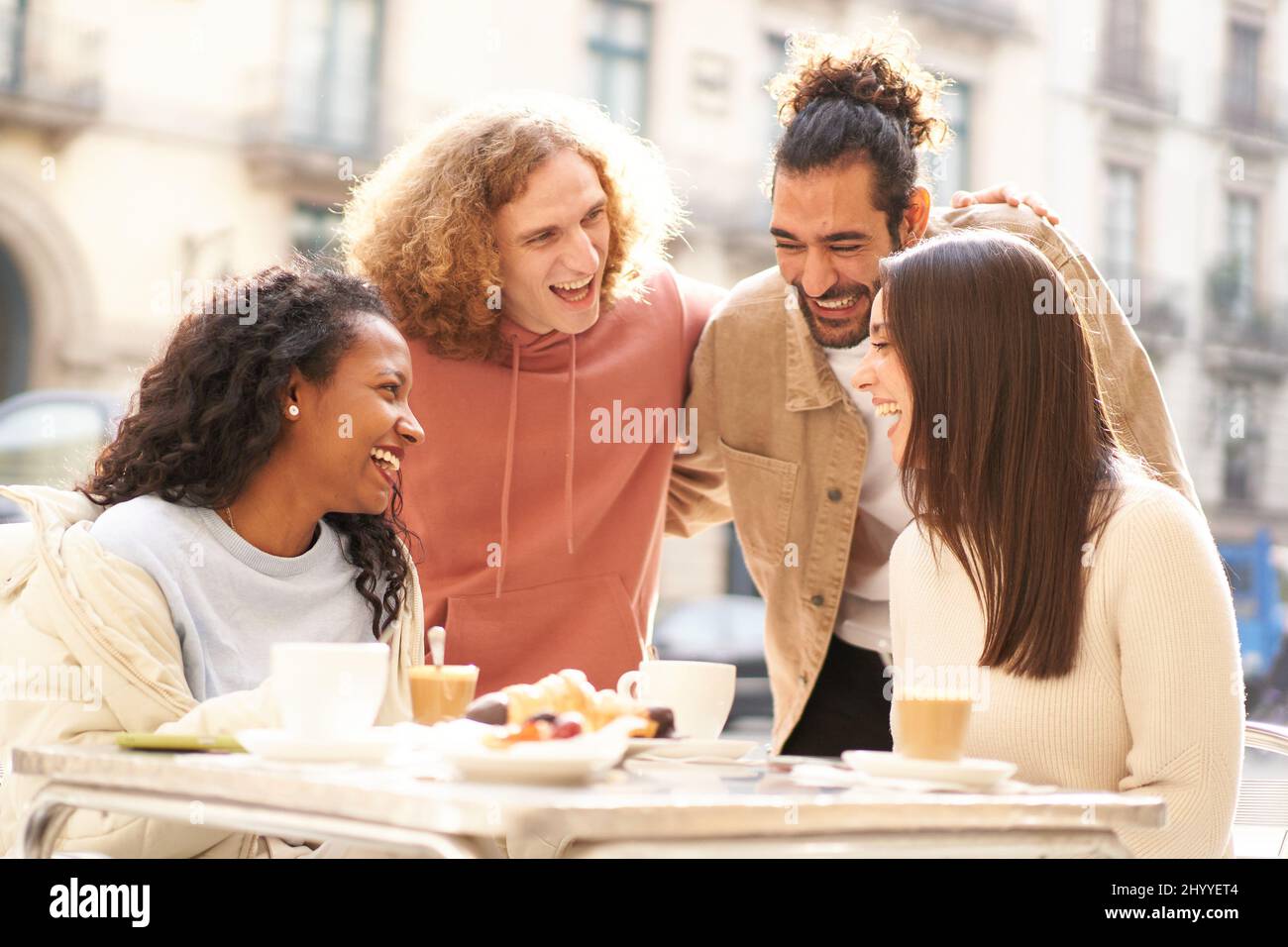 Zwei Freundinnen frühstücken auf der Terrasse der Bar, während 2 Jungs herüberkommen, um zu flirten. Stockfoto
