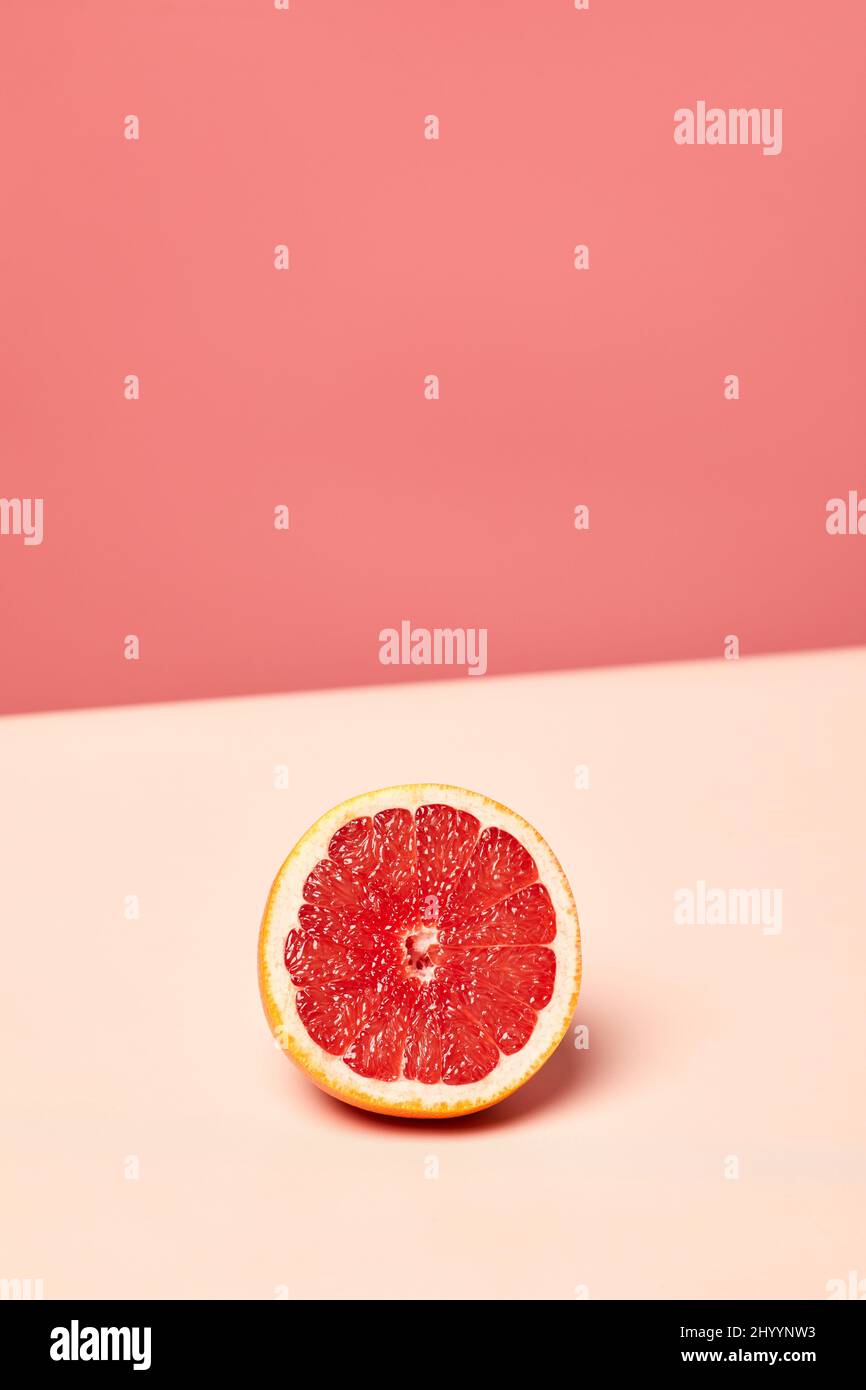 Minimales Hintergrundbild der Grapefruit-Hälfte auf rosa getöntem Hintergrund, Platz zum Kopieren Stockfoto