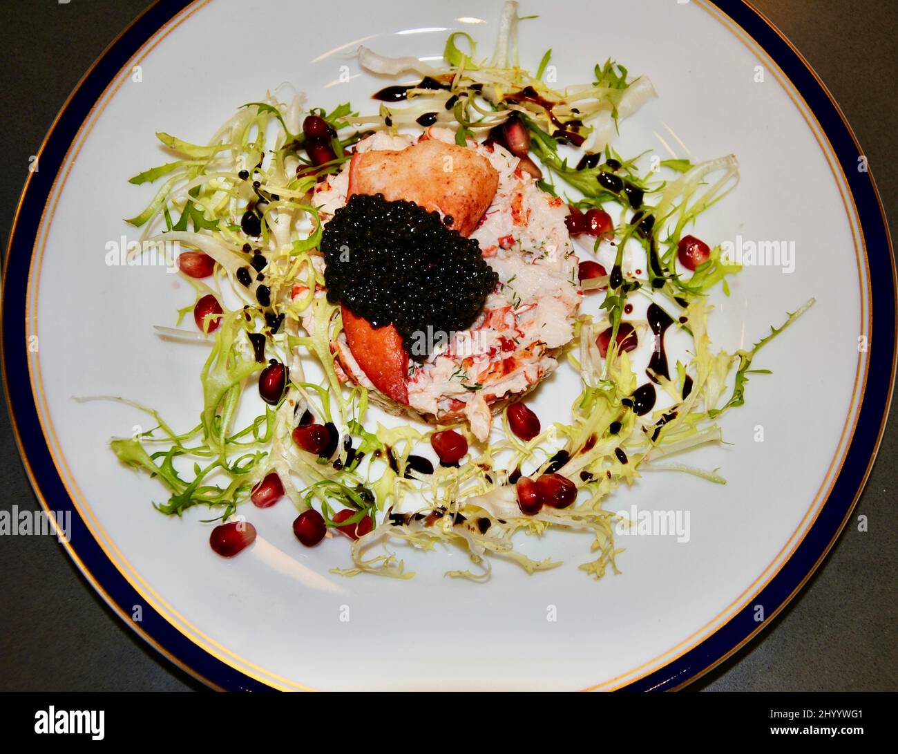 Hummersalat mit amerikanischem Paddelfischkaviar auf einem schönen Teller, der mit Frisée-Salat, Granatapfelkernen und Balsamico-Dressing verziert ist Stockfoto