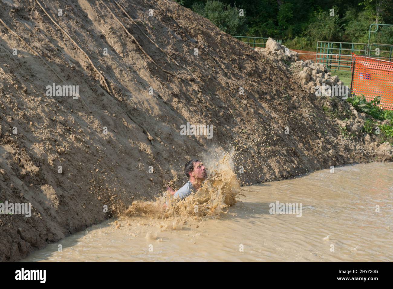 Ein männlicher Teilnehmer rutscht den schlammigen Hügel hinunter und macht beim Swampfoot Run einen Schrägstrich. Stockfoto