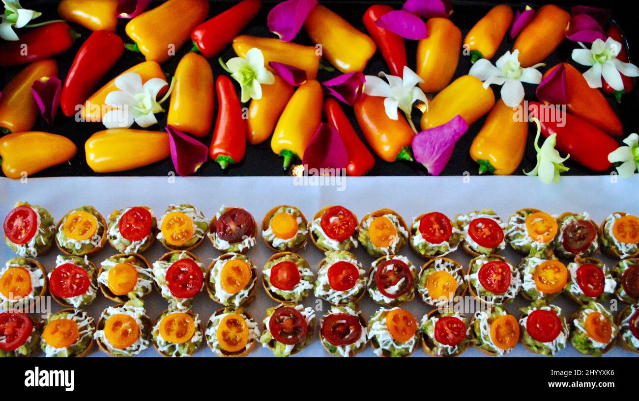 Cocktail-Hors d'Oeuvre, dekoriert mit bunten Scheiben von Mini-Tomate auf Tablett mit Mini-Paprika, weißen Orchideen und rosa Rosenblättern Stockfoto