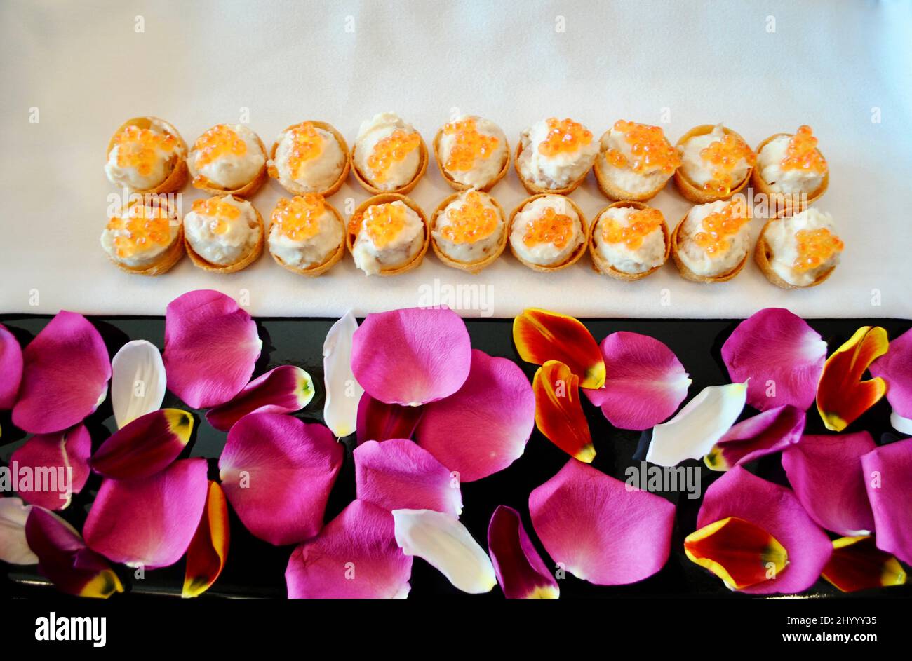 Geräucherter Weißfischsalat mit Lachskaviar als Cocktail-Hors d'Oeuvre auf einem Tablett, das mit rosa Rosenblättern und orangefarbenen Tulpenblättern verziert ist Stockfoto