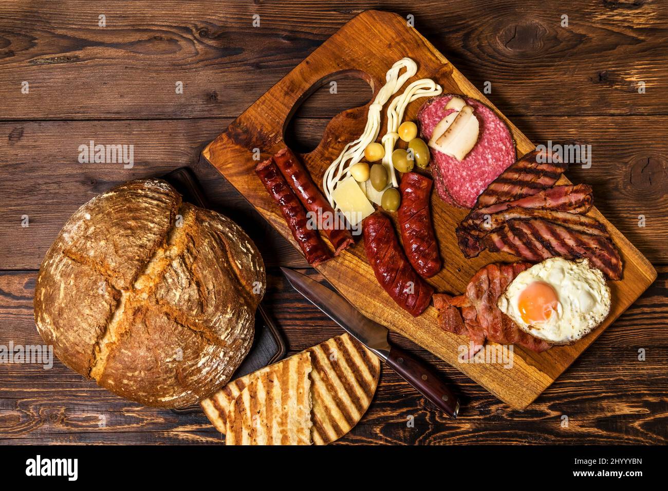 Verschiedene Arten von gegrillten Würstchen mit Ei. Eine Auswahl an gegrilltem Gourmet-Fleisch auf einem rustikalen Holzbrett. Gegrillte Würstchen mit hausgemachtem Brot. Stockfoto