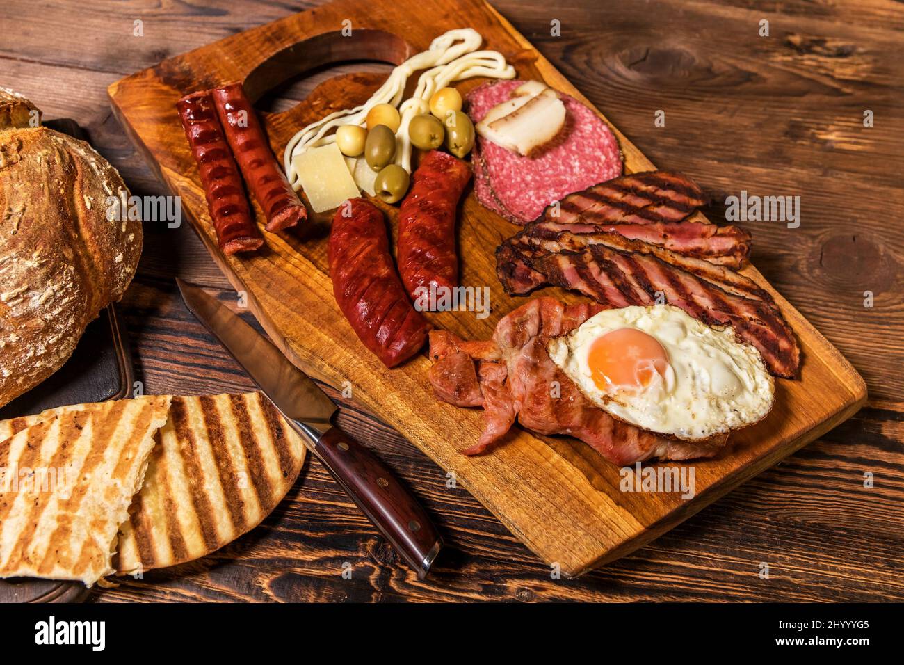 Verschiedene Arten von gegrillten Würstchen mit Ei. Eine Auswahl an gegrilltem Gourmet-Fleisch auf einem rustikalen Holzbrett. Gegrillte Würstchen mit hausgemachtem Brot. Stockfoto