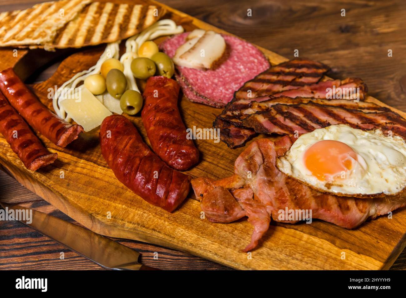 Verschiedene Arten von gegrillten Würstchen mit Ei. Eine Auswahl an gegrilltem Gourmet-Fleisch auf einem rustikalen Holzbrett. Gegrillte Würstchen mit hausgemachtem Brot. Stockfoto
