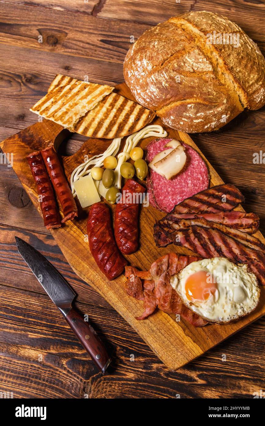 Verschiedene Arten von gegrillten Würstchen mit Ei. Eine Auswahl an gegrilltem Gourmet-Fleisch auf einem rustikalen Holzbrett. Gegrillte Würstchen mit hausgemachtem Brot. Stockfoto