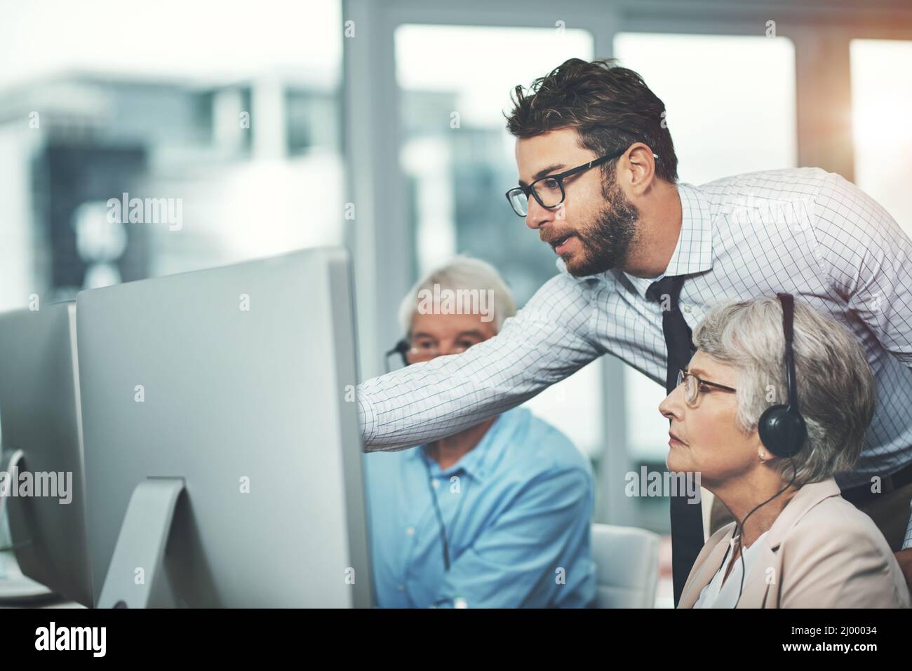 Es ist nie zu spät, einen neuen Beruf zu erlernen. Aufnahme eines jungen Mannes, der seinen älteren Kollegen in einem Callcenter hilft. Stockfoto