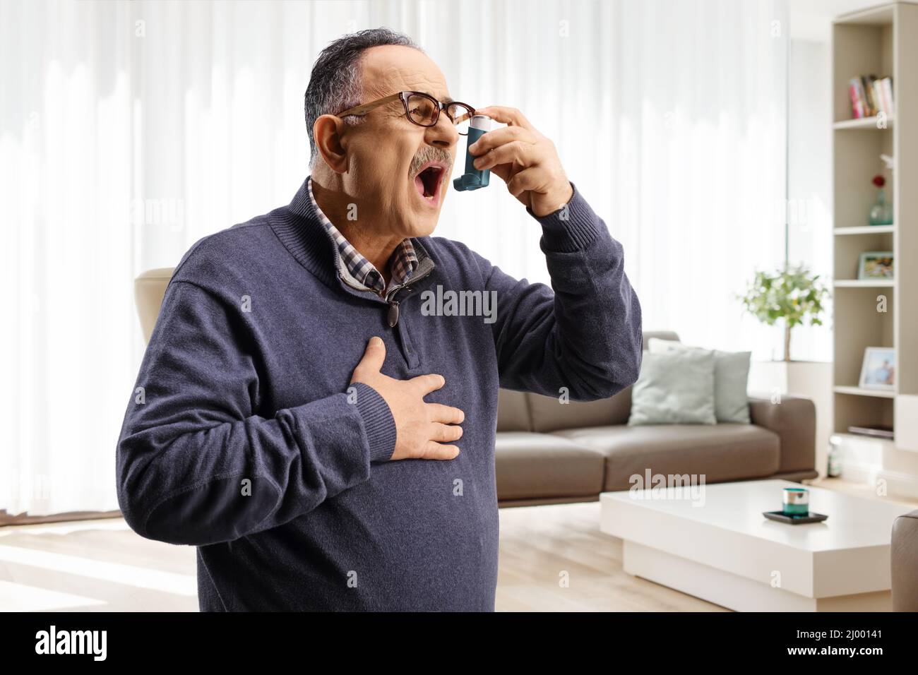 Reifer Mann mit einem Inhalator zu Hause in einem Wohnzimmer Stockfoto