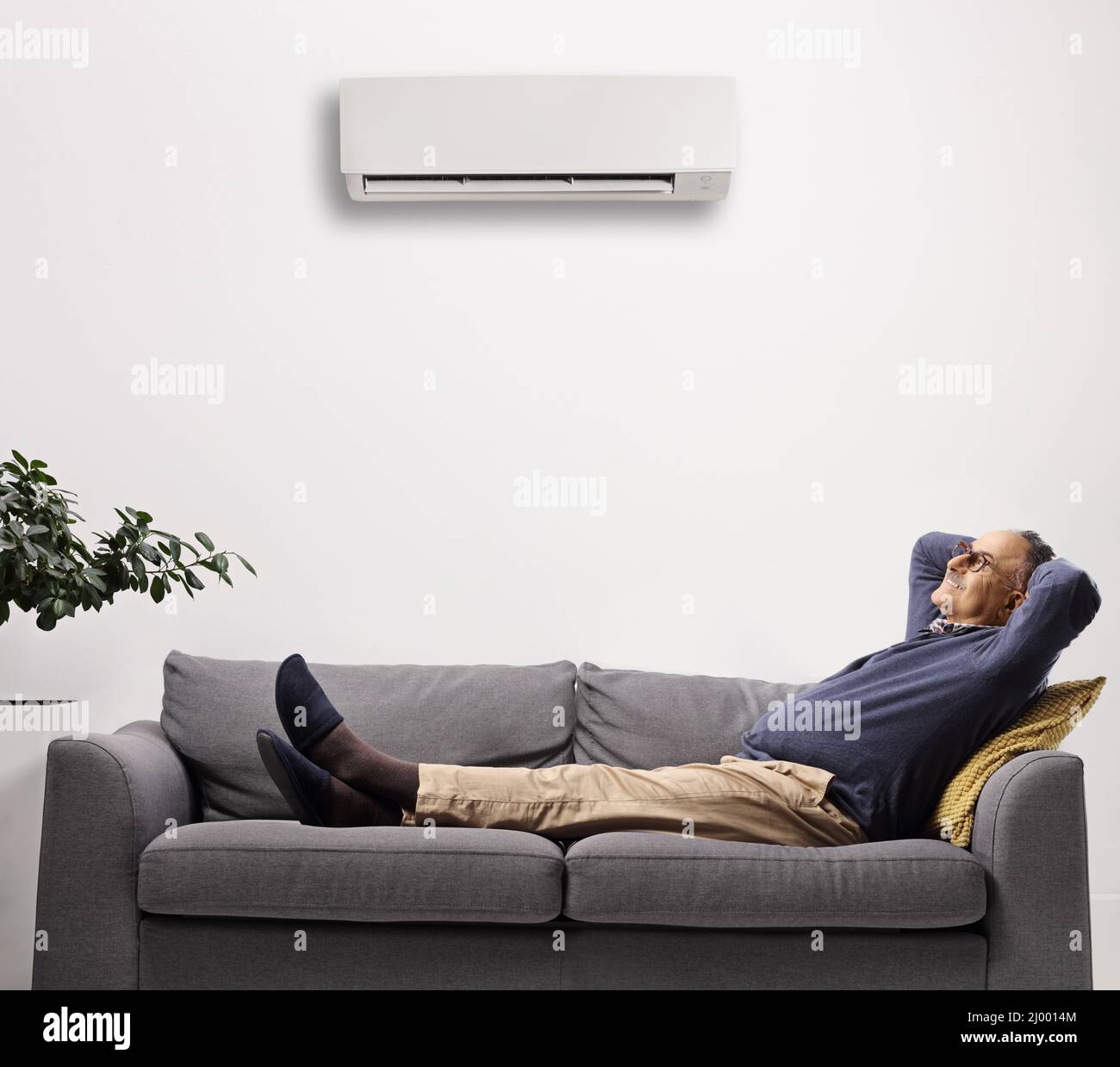 Reifer Mann ruht sich auf einem Sofa unter einer auf weißem Hintergrund isolierten Klimaanlage aus Stockfoto