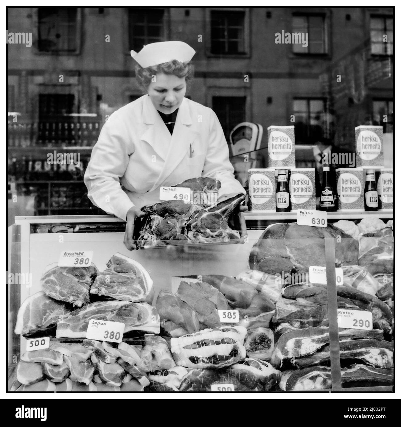 Vintage 1960s Helsinki Elanto's Fleischgeschäft, in dem Fleischstücke, die in finnischen Markka-Preisen berechnet wurden, in einem Schaufenster angeordnet sind. 1962 Helsinki, Uusimaa, Finnland Stockfoto