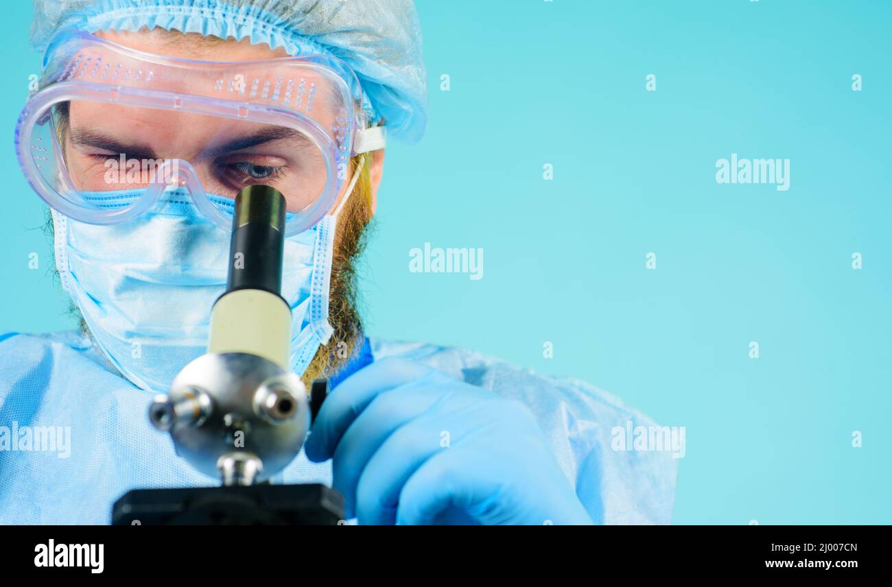 Arzt in medizinischer Maske mit Mikroskop. Mikrobiologe, der im Labor arbeitet. Medizinische Geräte. Stockfoto