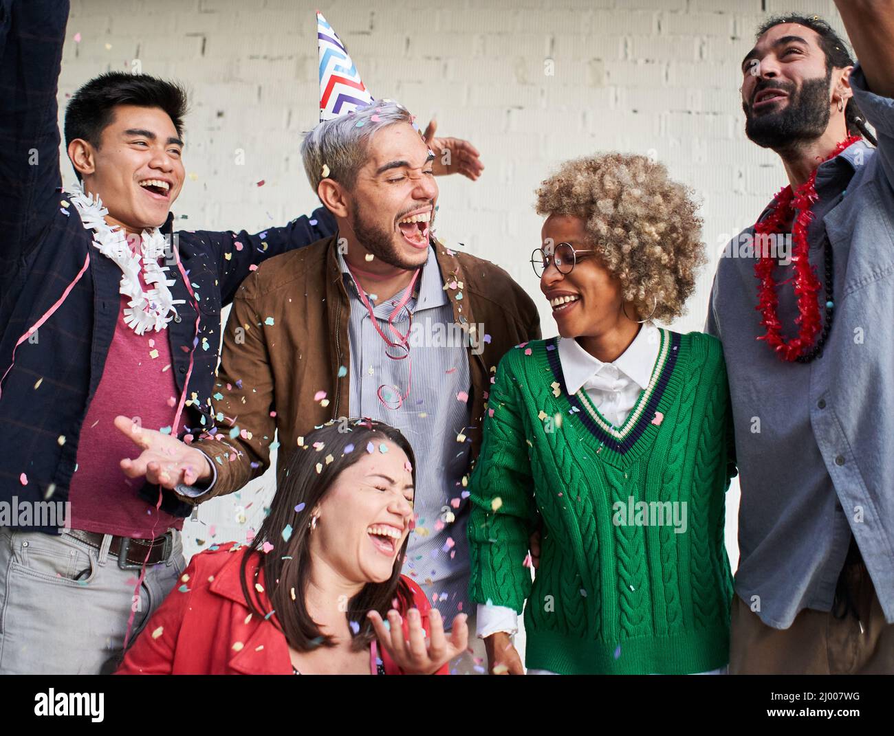 Junge Menschen blasen Konfetti aus den Händen. Freunde feiern Geburtstag im Freien. Stockfoto