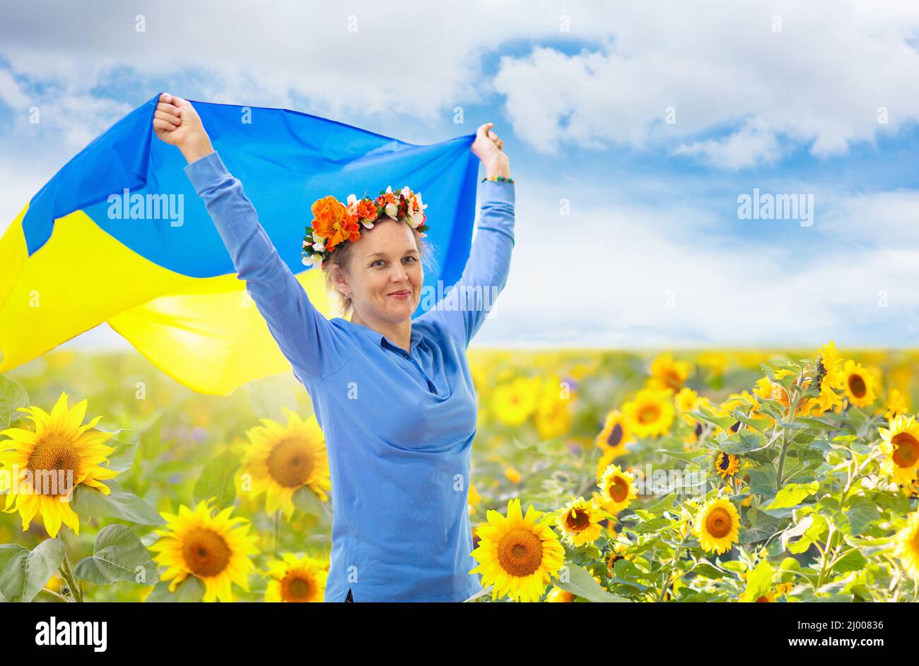 Betet für die Ukraine. Frau mit ukrainischer Flagge im Sonnenblumenfeld. Glückliche Frau winkt Nationalflagge und betet für den Frieden. Stockfoto