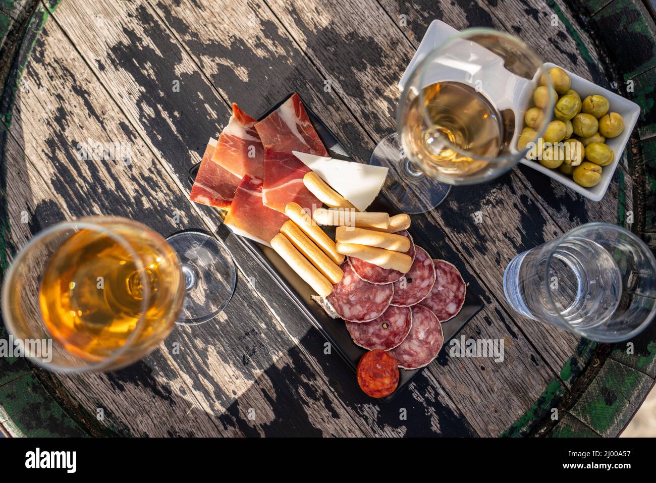 Spanische Tapas auf einem Holzfaßtisch mit zwei Gläsern Wein und einem Wasserglas. Oliven, Jamon, Chorizo, Käse. Stockfoto