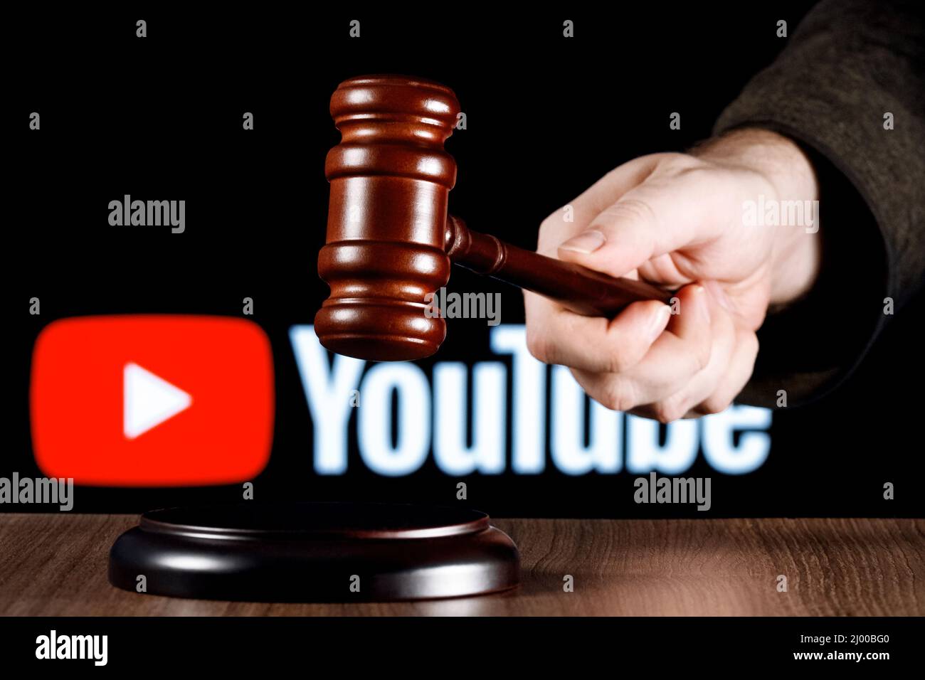 Gavel in Richterhand auf dem Tisch vor dem Hintergrund des Youtube-Logos. Das Konzept des Prozesses. Stockfoto