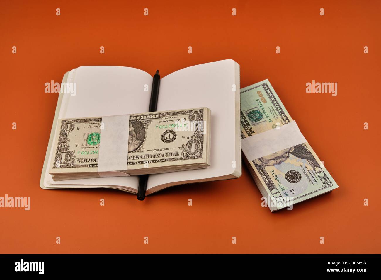 Notebook mit zwei Dollarpaketen auf einem orangefarbenen Tisch. Einsparungskonzept. Fotografieren Sie im horizontalen Format. Speicherplatz kopieren. Stockfoto