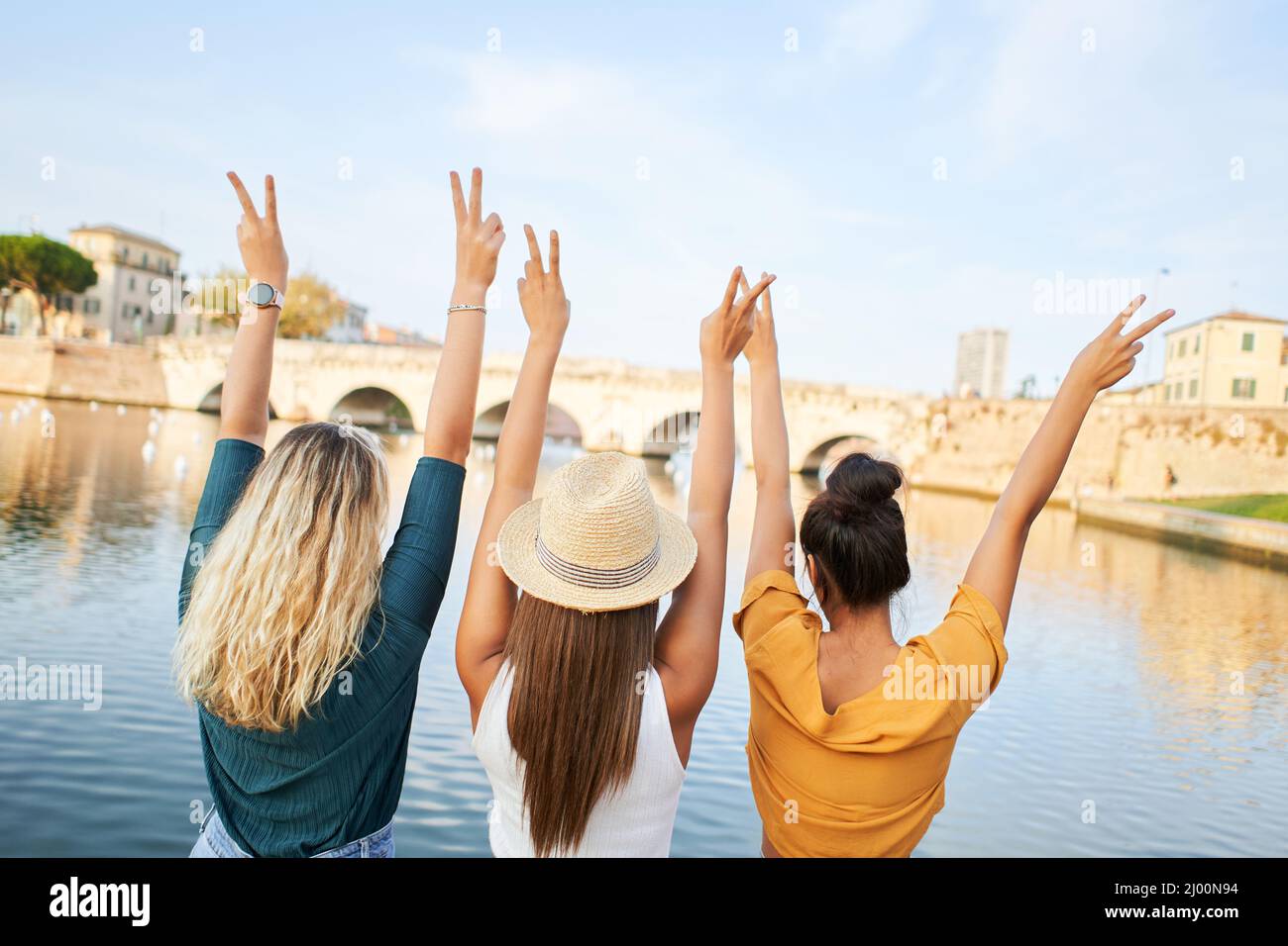 Rückansicht von glücklichen jungen Freundinnen, die mit erhobenen Händen auf dem See in der Resortstadt sitzen. Konzept von Tourismus und Freundschaft. Stockfoto