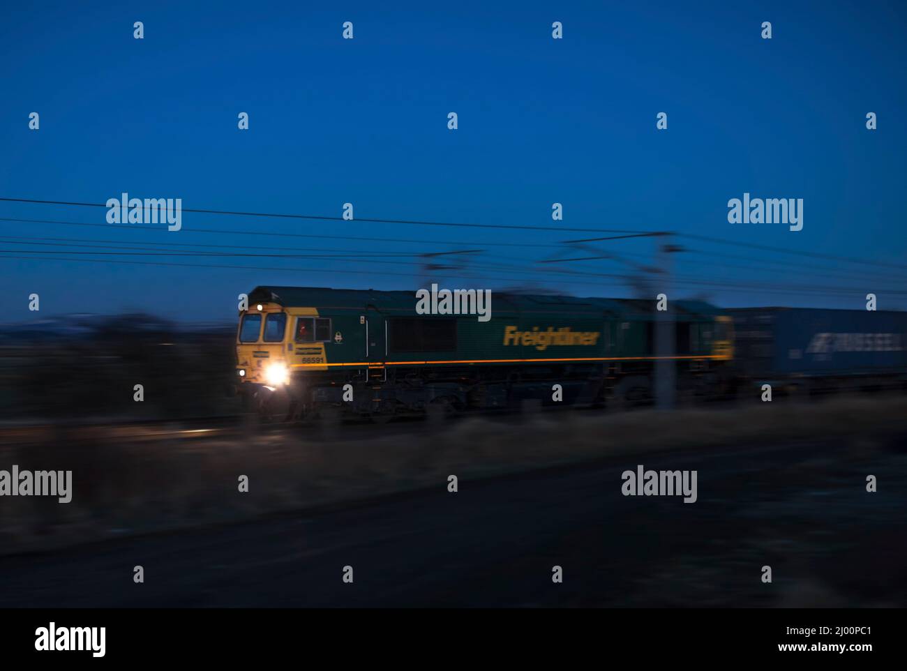 Freightliner EMD-Diesellokomotive der Baureihe 66 66591, die einen Containerzug auf der Hauptlinie der Westküste, Schottland, Großbritannien, schleppt, während der Dämmerung entlang fährt Stockfoto