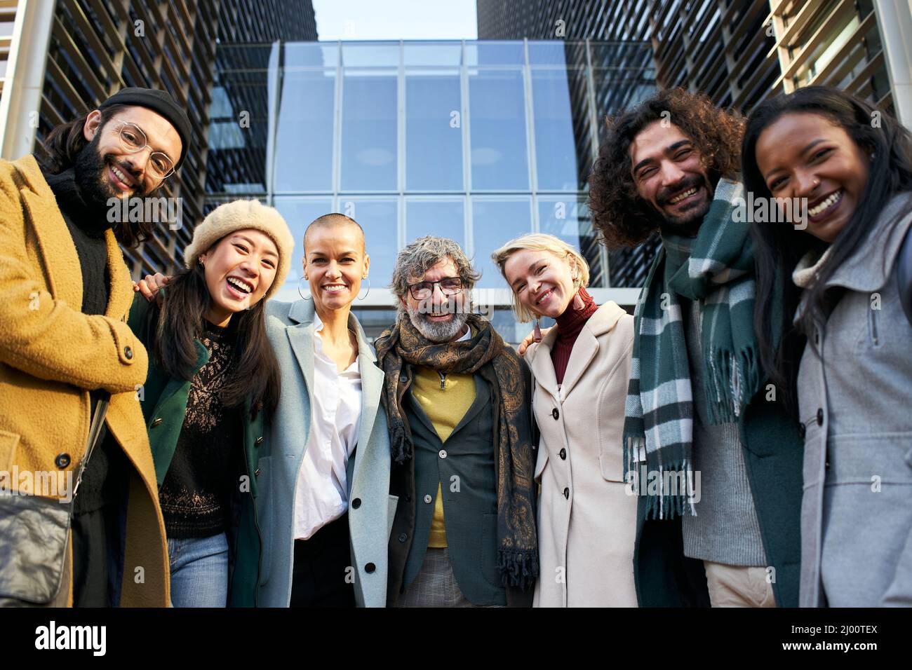 Porträt des Geschäftsteams beim Blick auf die Kamera lächelndes Porträt. Mann und Frauen im Freien zusammen in Gruppenfoto mit modernem Büro im Hintergrund Stockfoto