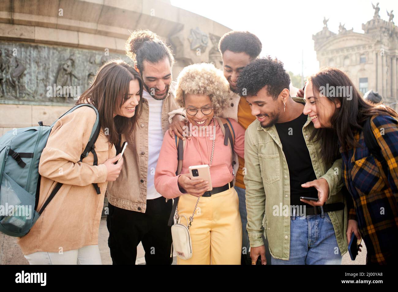 Eine Gruppe fröhlicher Freunde, die sich im Freien ein Smartphone ansehen. Menschen, die digitale Geräte nutzen und in sozialen Medien teilen, treffen zusammen. Stockfoto