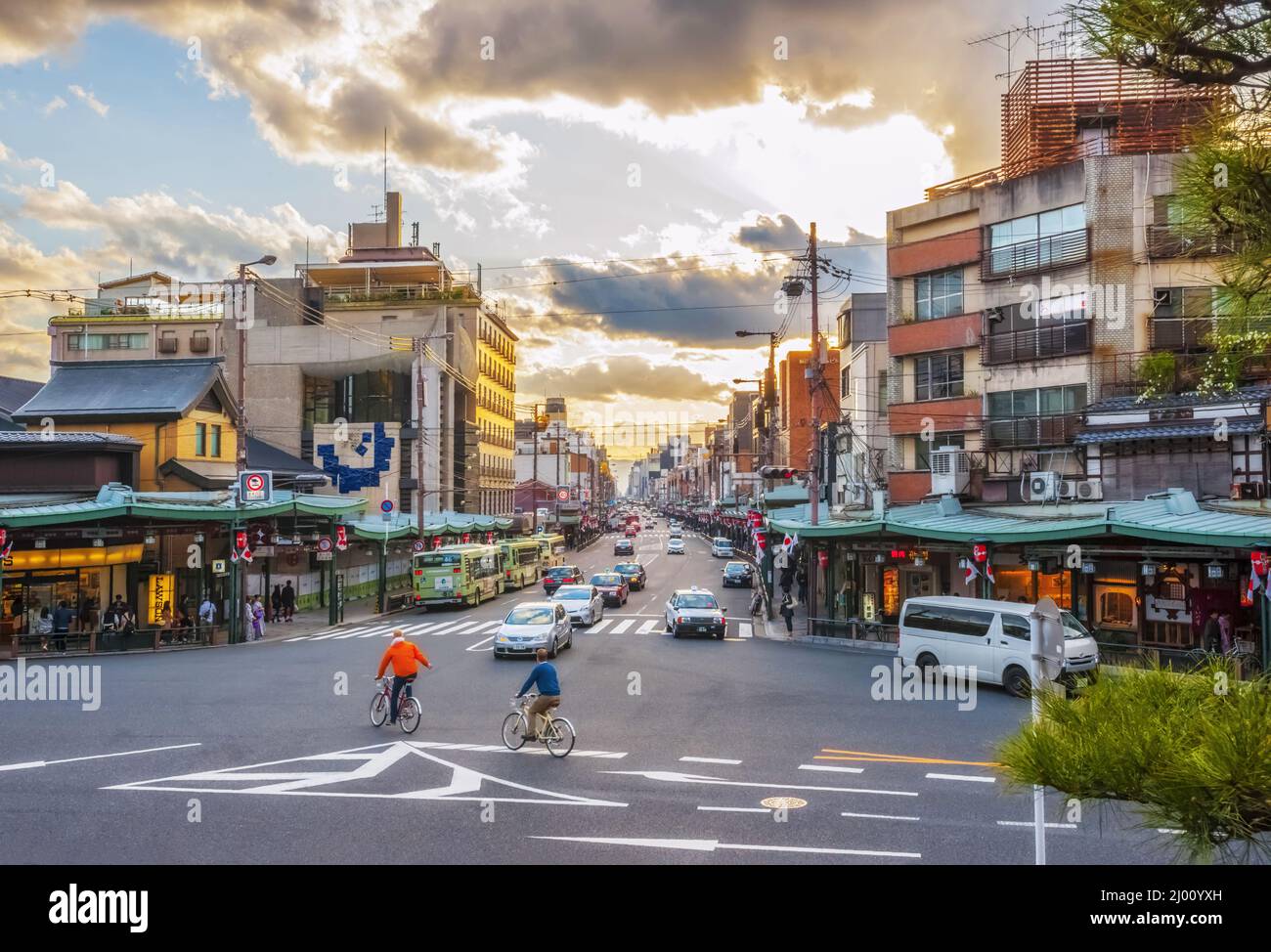 Shijo-dori in der Abenddämmerung mit Radfahrern, Fahrzeugen, Ampeln und einem warmen Leuchten der untergehenden Sonne vom Nishiromon-Tor aus gesehen, Gion, Kyoto, Japan Stockfoto