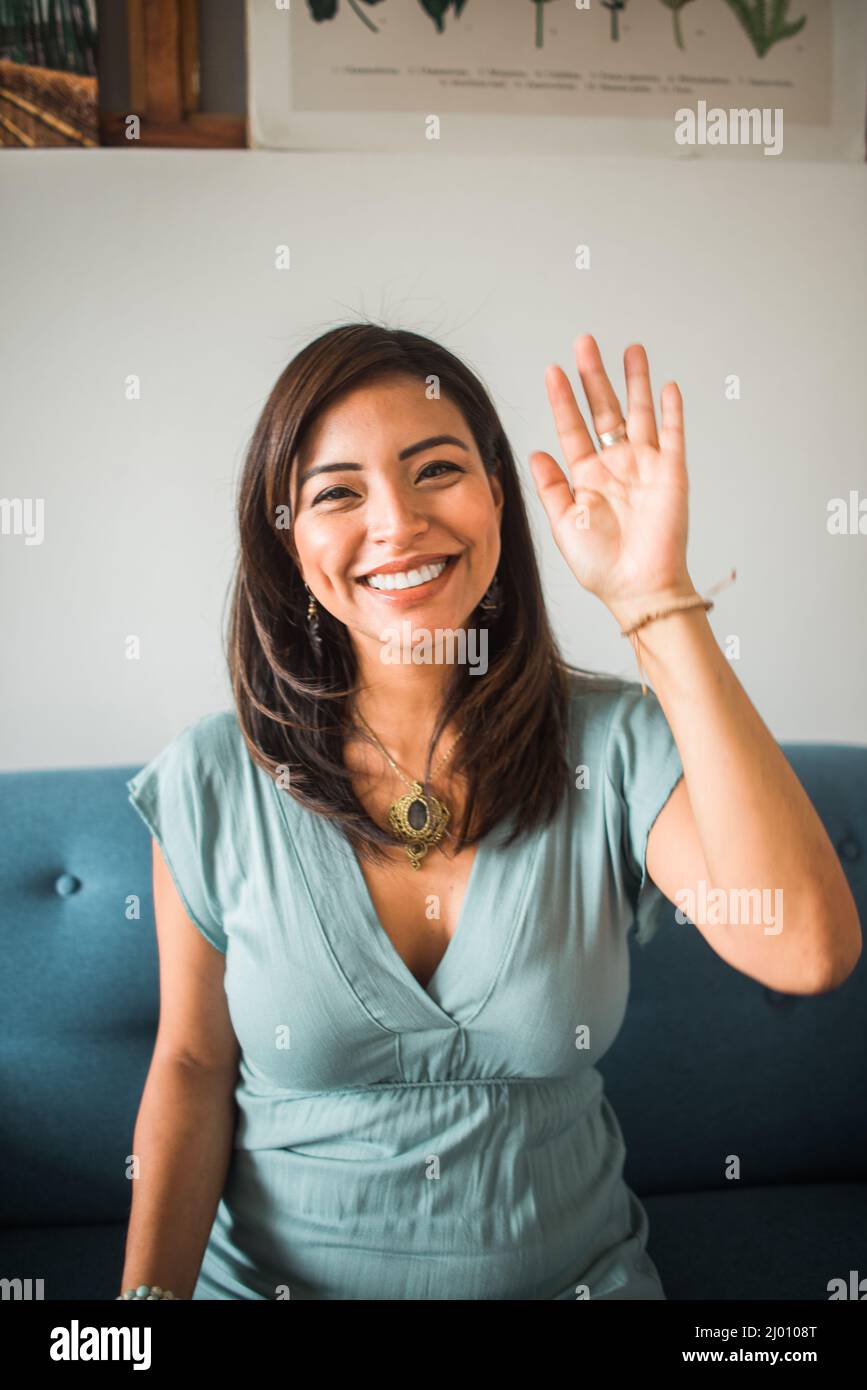 Vertikales Porträt einer Frau, die die Kamera in ihrem Wohnzimmer zu Hause anwinkt und lächelt Stockfoto