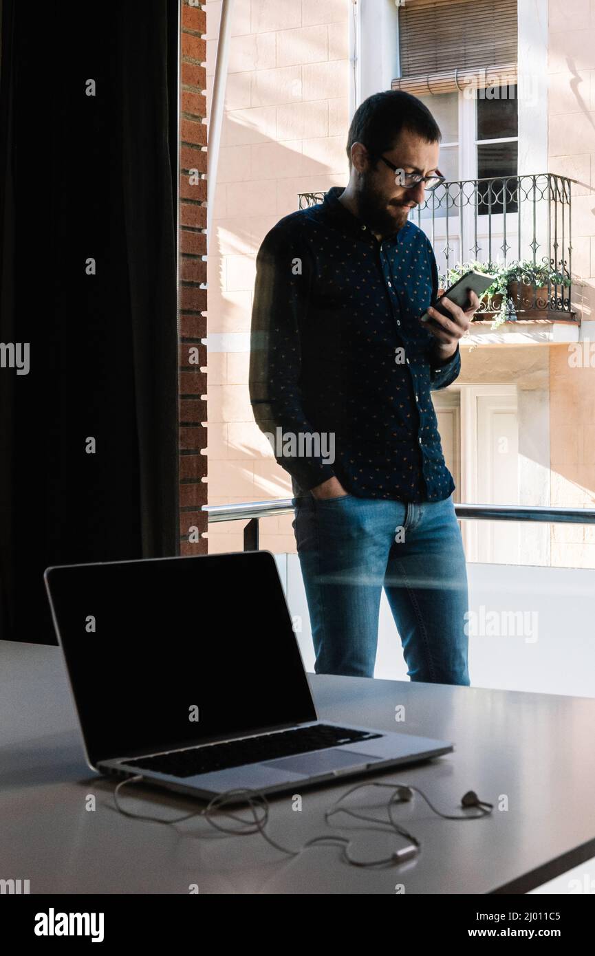 Mann macht eine Pause von der Telearbeit, indem er sein Smartphone anschaut Stockfoto