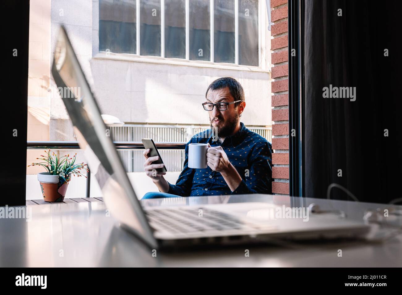 Mann macht eine Pause von der Telearbeit, indem er sein Smartphone anschaut Stockfoto