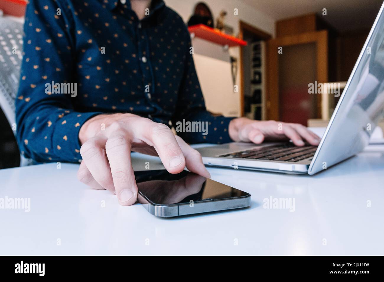 Nahaufnahme der Hände eines Mannes mit Laptop, der das Smartphone überprüft Stockfoto