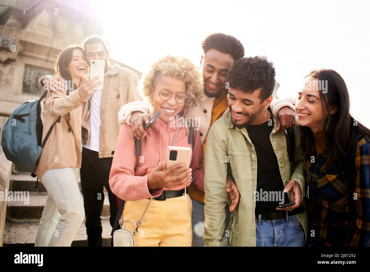 Eine Gruppe fröhlicher Freunde, die sich im Freien ein Smartphone ansehen. Menschen, die digitale Geräte nutzen und in sozialen Medien teilen, treffen zusammen. Stockfoto