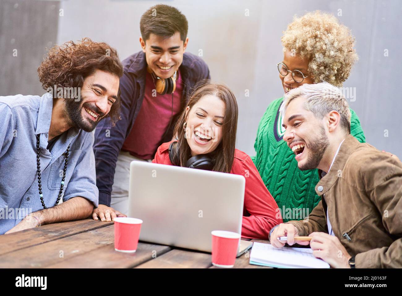 Eine Gruppe junger Studenten, die sich ein Video auf dem Laptop im Freien ansehen. Millennial lächelnde Menschen mit Laptop für Videoanruf Stockfoto