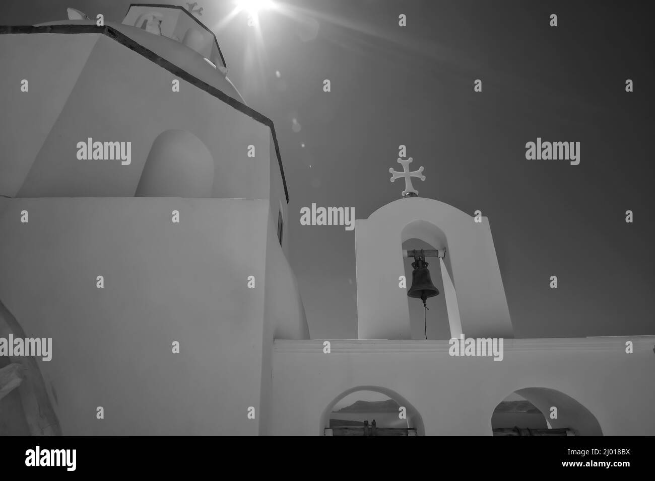 Niedrige Ansicht einer weiß getünchten Kirche mit Glocken, einem Kruzifix und Sonnensternen oben am Himmel in schwarz-weiß Stockfoto