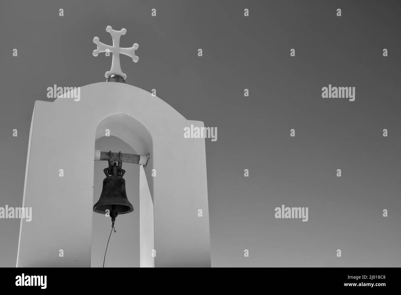 Eine Kirchenglocke und ein Kreuz auf der Spitze einer griechisch-orthodoxen Kirche und ein wunderschöner blauer Himmel auf Santorin in Schwarz und Weiß Stockfoto