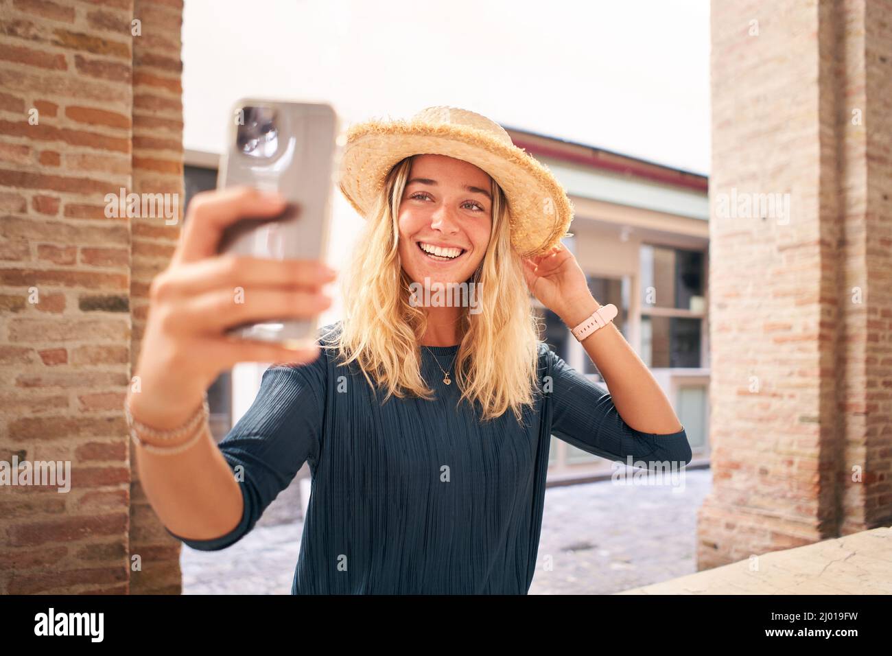 Schöne glückliche Frau in Sommerkleidung, die lächelndes Selfie trägt Hut. Weibliche Blondine mit Handy. Social Media Stockfoto