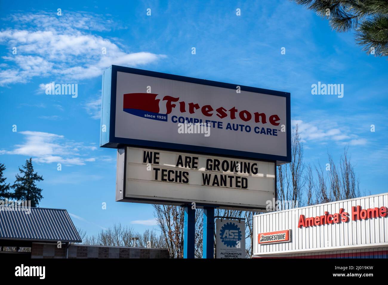 Woodinville, WA USA - ca. Februar 2022: Low-Angle-Ansicht eines Now Hiring-Zeichens an einem Firestone Auto Care an einem hellen sonnigen Tag. Stockfoto