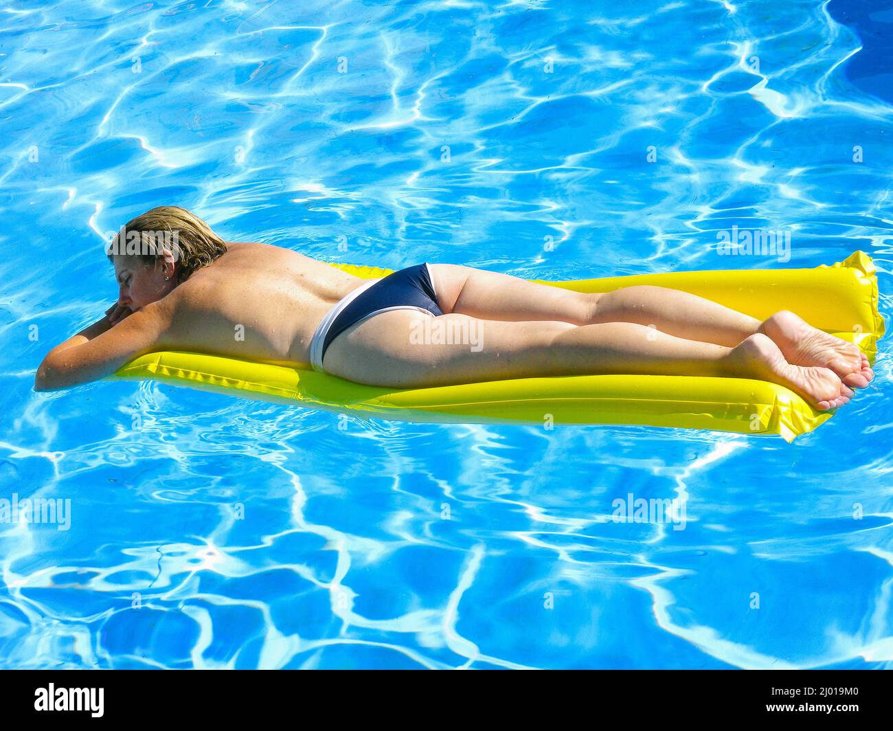 Kaukasische reife Frau liegt auf einer gelben aufblasbaren Matratze und sonnt sich in einem Schwimmbad Stockfoto