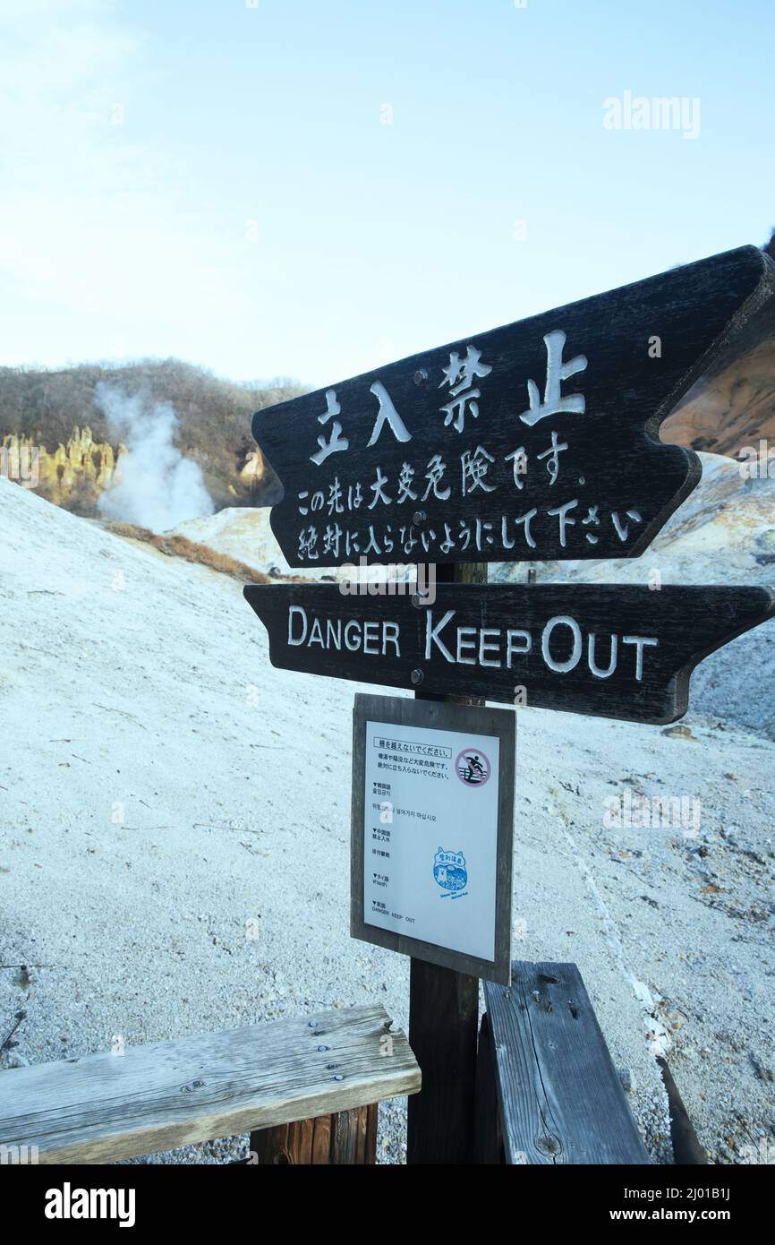 Nahaufnahme eines hölzernen schwarzen Schildes mit einem japanischen Text GEFAHR HALTEN Warnung mit Schnee hinter Stockfoto