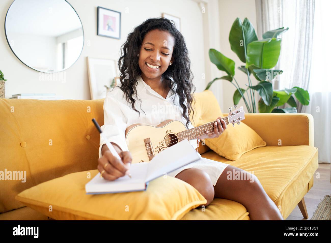 Sängerin und Songwriterin komponiert zu Hause ein Lied. Musikkünstler schaffen. Mädchen, das ein Lied in einem Notizbuch auf dem Sofa schreibt. Stockfoto