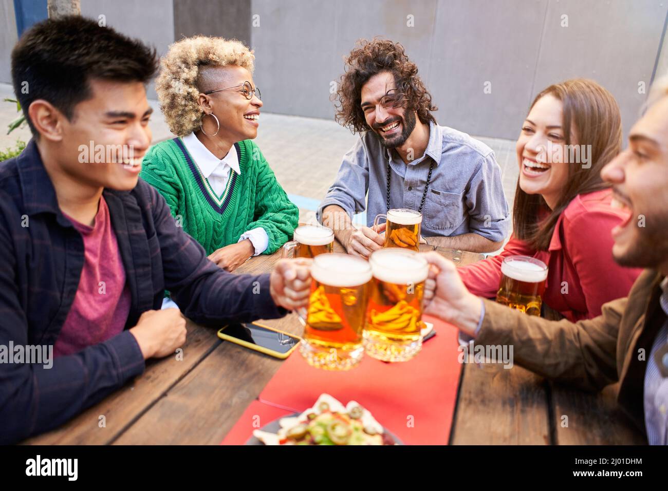 Fröhliche Leute, die beim Biertrinken auf der Terrasse beim Abendessen Spaß hatten. Junge Freunde essen gemeinsam im Restaurant. Stockfoto