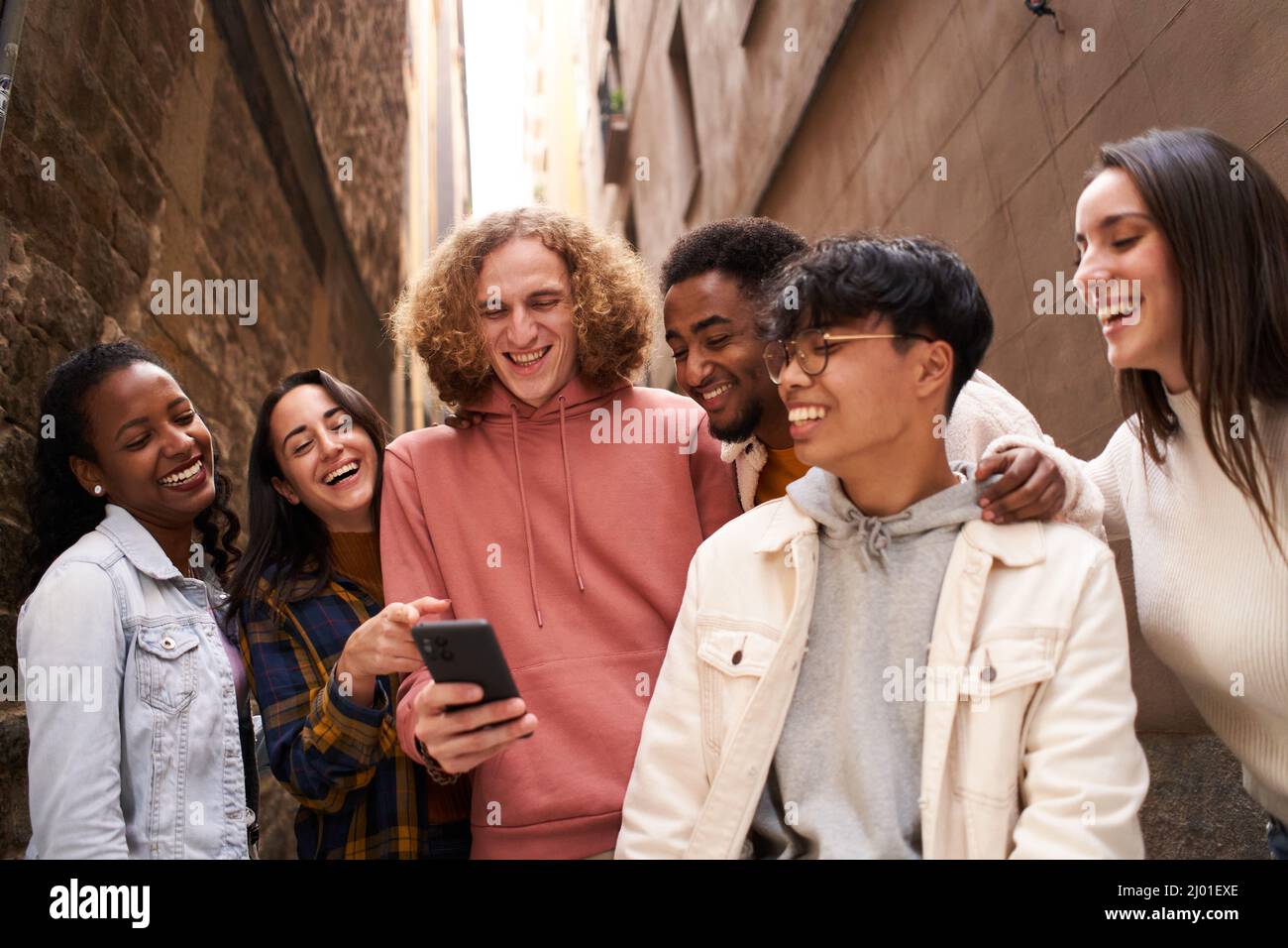 Gruppe von glücklichen jungen Teenagern, die im Freien Smartphone benutzen, während sie sich etwas im Handy ansehen und lachen. Konzept der Technologie, Freundschaft und Stockfoto