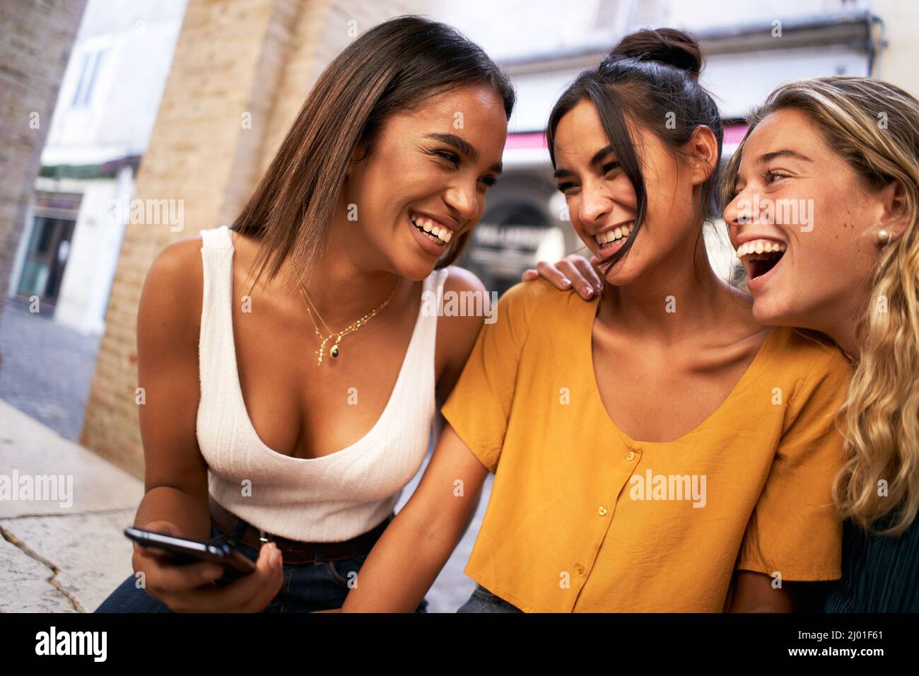 Portrait von ziemlich charmanten multirassischen Frauen lachen beim Lesen von Nachrichten oder sms mit Handys im Freien. Stockfoto