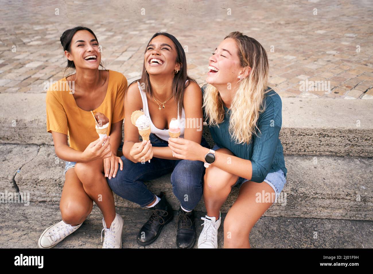 Drei junge Frauen essen Eiszapfen und lachen gut heißen Sommertag während ihres Urlaubs. Fröhliche Menschen, die lächeln Stockfoto