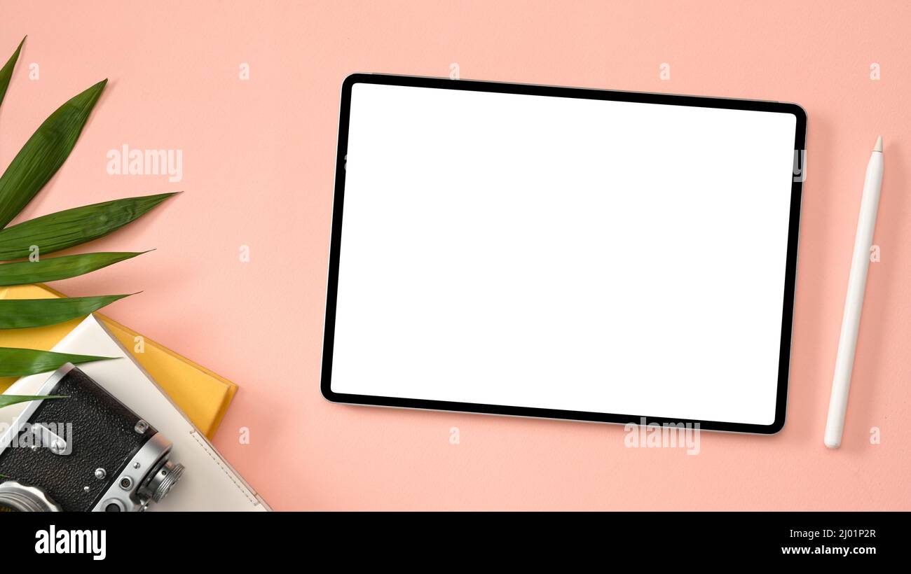 Draufsicht, Arbeitsbereich des Travel Bloggers mit weißem Digital Tablet-Mockup, Eingabestift, Kamera und Zubehör auf rosa Hintergrund. Stockfoto