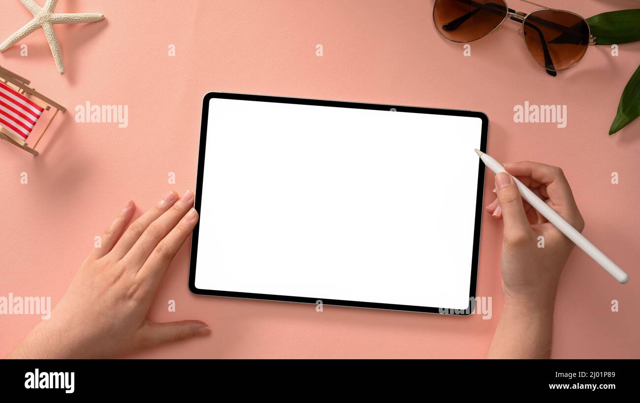 Die Hände einer freiberuflichen Frau verwenden einen Stylus, um ein Grafikbild auf einem Tablet-Bildschirm vor einem eleganten rosa Büroschreibtischhintergrund zu entwerfen. Draufsicht Stockfoto