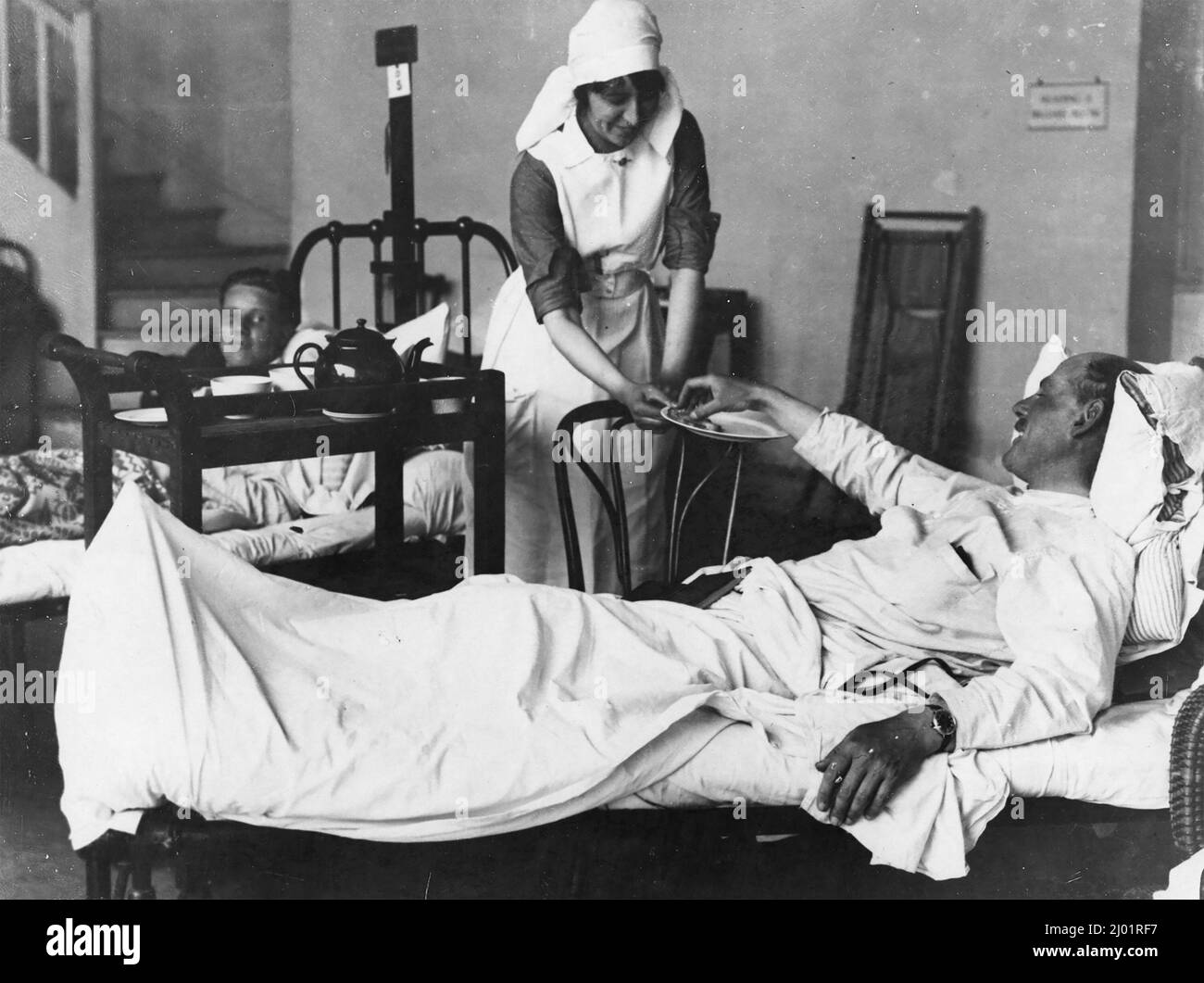 Verwundete Soldaten, die im Jahr WW1 in einem Krankenhausbett lagen. Ihm wird von einer Krankenschwester ein Teller mit Keksen angeboten. Stockfoto
