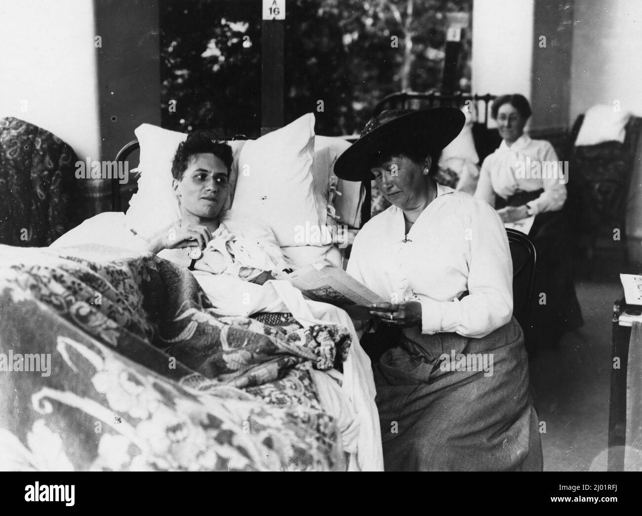 Verwundete Soldaten liegen in einem Krankenhausbett. Nach der Originalunterschrift ist die Frau, die neben ihm sitzt, seine Mutter. Sie liest, möglicherweise laut, aus einer Zeitschrift. Direkt hinter ihnen sitzt eine andere Frau neben einem Bett. Stockfoto