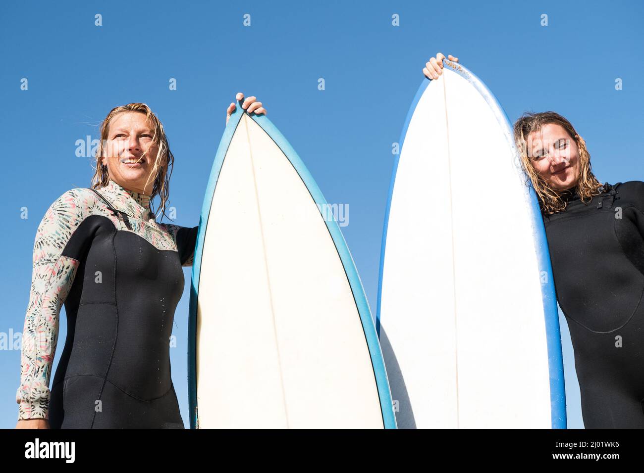 2 kaukasische Surferinnen im Portrait stehend mit Surfbrettern. Sie tragen Winternassanzüge Stockfoto