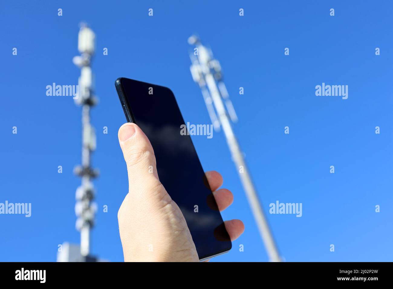 Smartphone in der Hand auf dem Hintergrund von Zelltürmen. Mobilkommunikationsgeräte, Signalstärke des Telefons Stockfoto